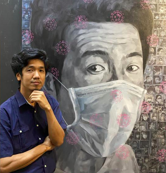 Portrait of the Burmese painter Khin Zaw Latt posing in front of his self-portrait taken during covid, with a mask on the face.